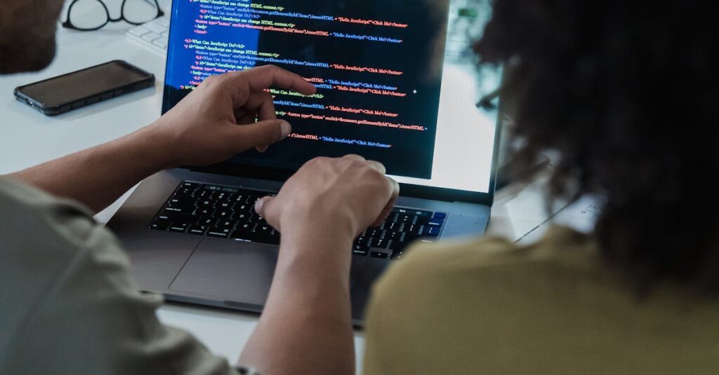 Two adults collaborating on programming tasks using a laptop in an office setting.